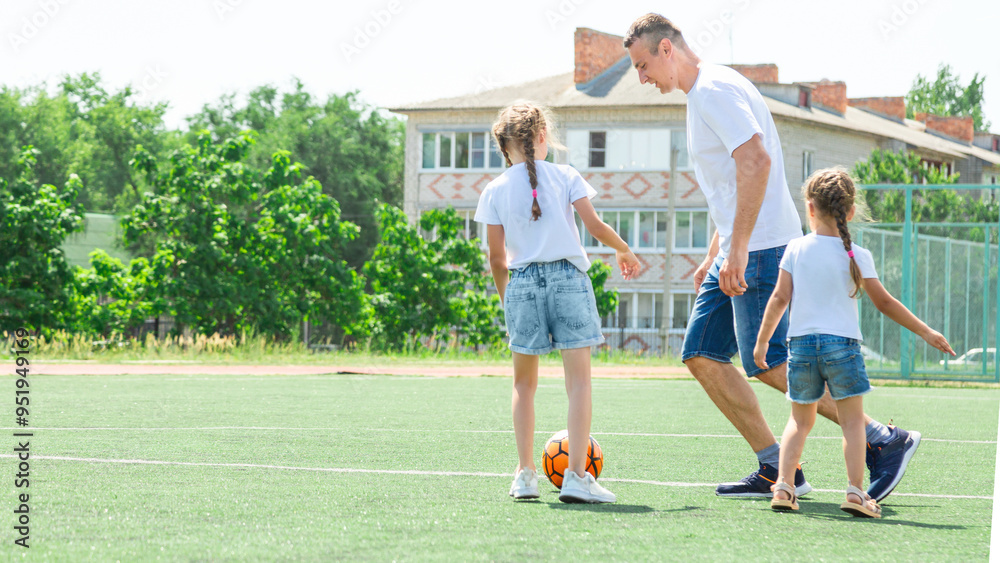 Obraz premium Father and daughters play football. Dad and little girls play soccer. Young active family enjoy sunny summer day outdoor. Healthy sport for kids. Football game club.