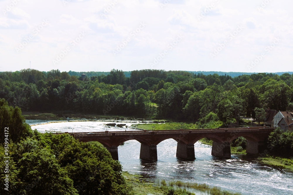 Fototapeta premium top view of an old red brick bridge over a river with a forest in the background