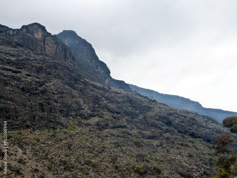 View of Mount Kilimanjaro peak in Tanzania and rocky slopes overgrown with sparse vegetation and bushes. Tourist route and nature View of Mount Kilimanjaro peak in Tanzania and rocky slopes overgrown with sparse vegetation and bushes. Tourist route and nature