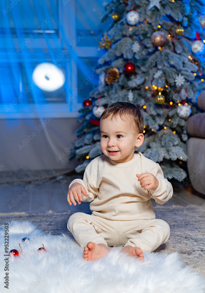 Joyful toddler playing near a decorated Christmas tree indoors. A joyful toddler plays with ornaments on a soft rug next to a beautifully decorated Christmas tree