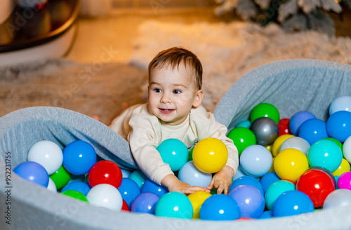Toddler playing joyfully in colorful ball pit at home in the evening. A happy toddler enjoys playing in a vibrant ball pit filled with various colored balls
