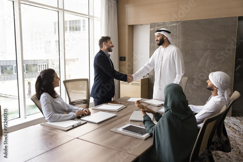 Photography Positive confident Arab and European businessmen shaking hands at team meeting,