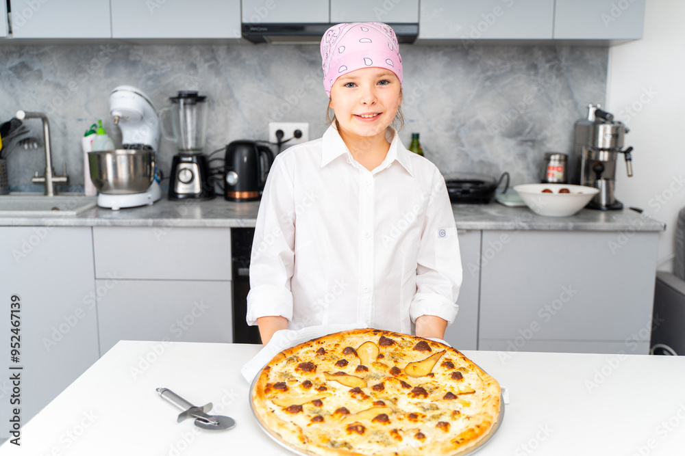 A little teenage girl holds a pizza with cheese and pear, baked for her at home in the kitchen. A little teenage girl holds a pizza with cheese and pear, baked for her at home in the kitchen.