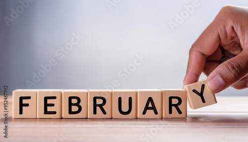 A hand is holding a block of wood with the letters "FEBRUARY" on it