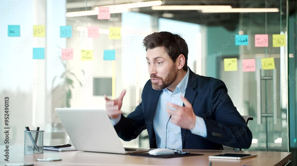 Angry dissatisfied businessman in a formal suit arguing on a video call using a laptop sitting at workplace in business office. Excited man boss emotionally talks with a subordinate about problems Angry dissatisfied businessman in a formal suit arguing on a video call using a laptop sitting at workplace in business office. Excited man boss emotionally talks with a subordinate about problems