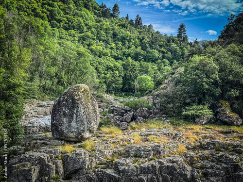 Big round rock standing on rocky ground in a green valley at the junction of the Altier and Chassezac rivers in the Cevennes, Lozère, France. photo