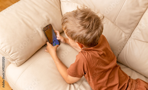 Close up of teenage boy playing mobile game online via smartphone sitting on sofa