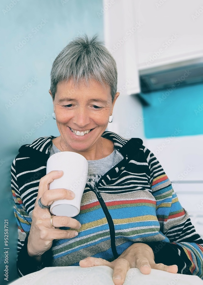 Smiling young woman sitting in the kitchen reading a book with a cup in her hand.Woman reading with a cup of coffee in her hand.Girl relaxing reading a book and drinking a cup of tea. Smiling young woman sitting in the kitchen reading a book with a cup in her hand.Woman reading with a cup of coffee in her hand.Girl relaxing reading a book and drinking a cup of tea.