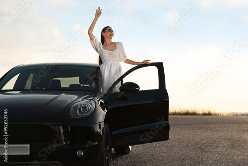 Smiling young woman in sunglasses leaning out of car outdoors. Enjoying trip