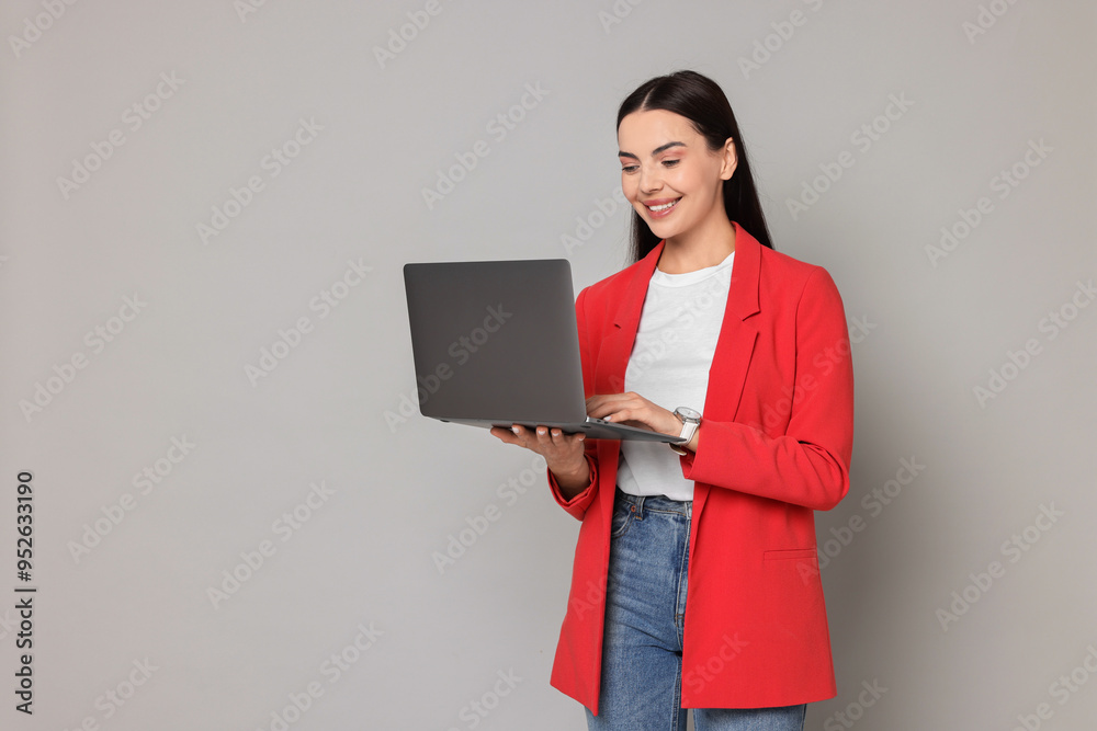 Beautiful woman in red jacket using laptop on gray background, space for text Beautiful woman in red jacket using laptop on gray background, space for text