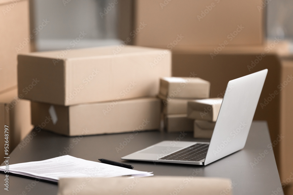 Organized home office warehouse workspace for processing shipments, managing shipping, storage, orders or logistics. Close up open laptop on desk, nearby stacks of cardboard boxes of various sizes Organized home office warehouse workspace for processing shipments, managing shipping, storage, orders or logistics. Close up open laptop on desk, nearby stacks of cardboard boxes of various sizes