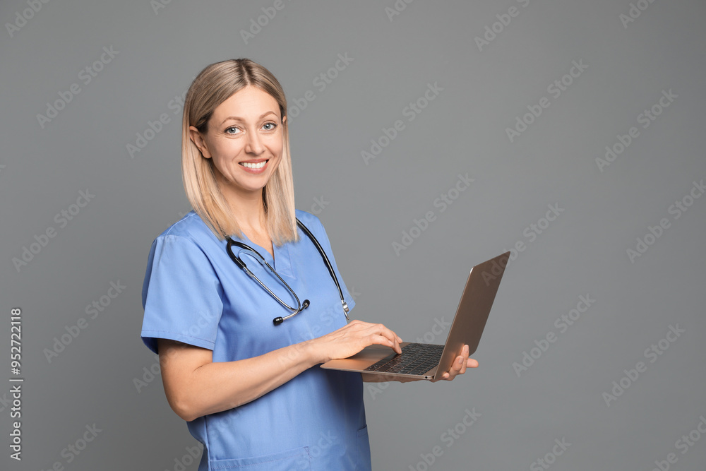 Doctor in medical uniform with stethoscope using laptop on grey background Doctor in medical uniform with stethoscope using laptop on grey background