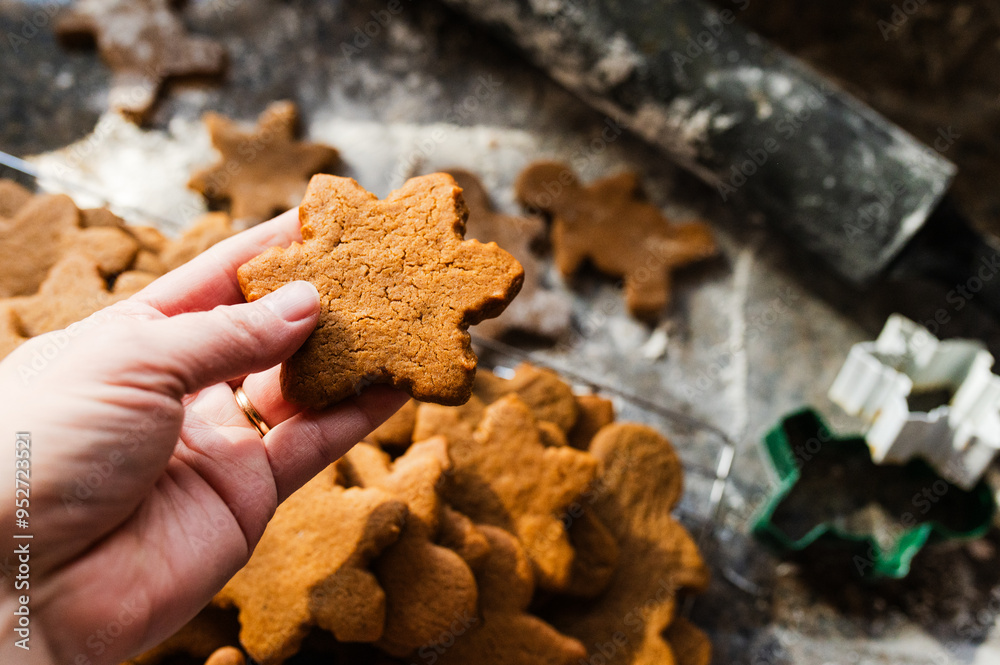 Hand holding a freshly baked gingerbread cookie over a cooling rack