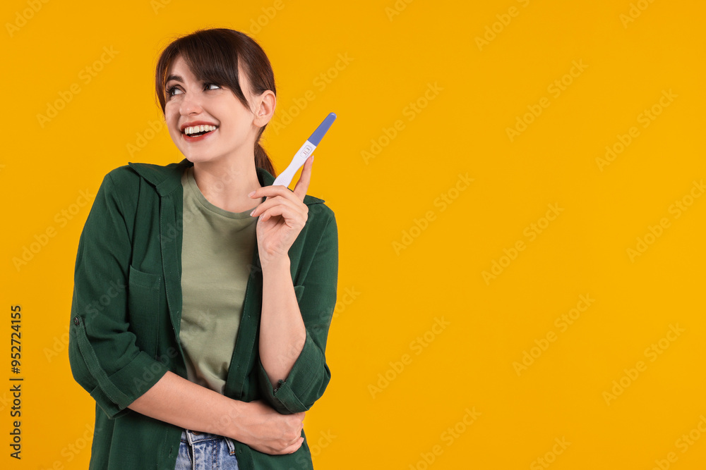 Happy young woman with pregnancy test on orange background, space for text Happy young woman with pregnancy test on orange background, space for text