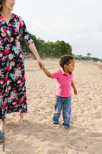 Toddler diverse racially holding moms hand on beach in lake photo