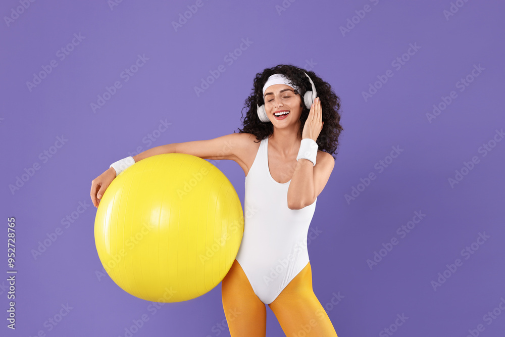 Aerobics. Happy woman in headphones with fitness ball on purple background Aerobics. Happy woman in headphones with fitness ball on purple background