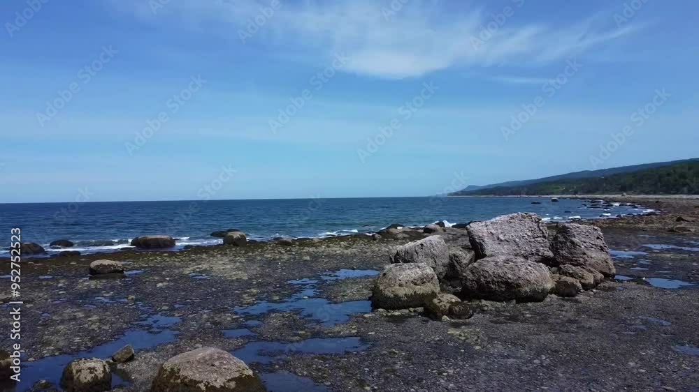 Vol de drone contournant un amas de gros rochers reposant sur le rivage d'une plage a marée basse frappé par les vagues bordée d'une forêt verdoyante. ( Grosses-Roches, Québec, Canada ) Vol de drone contournant un amas de gros rochers reposant sur le rivage d'une plage a marée basse frappé par les vagues bordée d'une forêt verdoyante. ( Grosses-Roches, Québec, Canada )