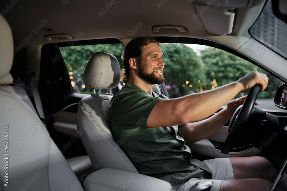 Smiling man driving a car in a modern urban setting with green trees in the background Smiling man driving a car in a modern urban setting with green trees in the background
