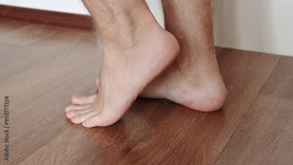 Legs of caucasian man doing exercises and standing on tiptoes alternately. Warm up workout and strengthening of foot muscles during independent exercises at home on floor. Legs of caucasian man doing exercises and standing on tiptoes alternately. Warm up workout and strengthening of foot muscles during independent exercises at home on floor.