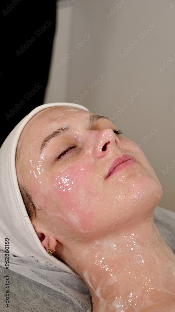 professional cosmetologist applies a white mask on the face of a female client with a brush, close-up professional cosmetologist applies a white mask on the face of a female client with a brush, close-up