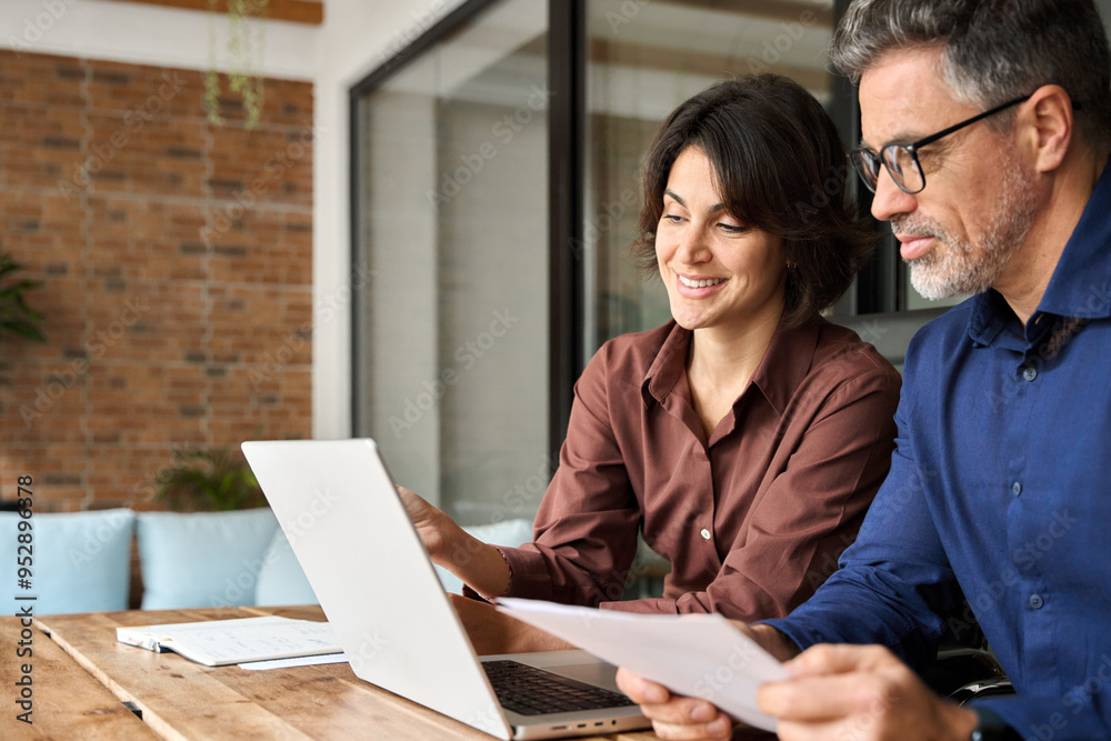 © insta_photos - Two busy professionals man and woman business executives checking document working together on laptop in office. Financial advisor manager lawyer and investor discussing corporate project at meeting.