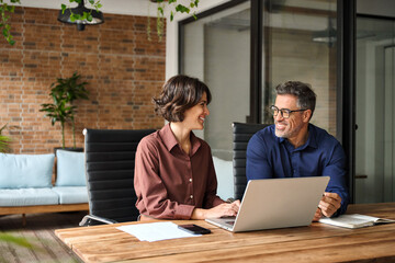Two happy busy professional executives team business people working together on laptop computer in modern office at corporate meeting. Professional bank manager consulting company client at work.