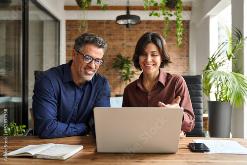 Two busy happy professional business man and woman executive leaders team using laptop working on computer at work desk having conversation on financial project at meeting in office. photo