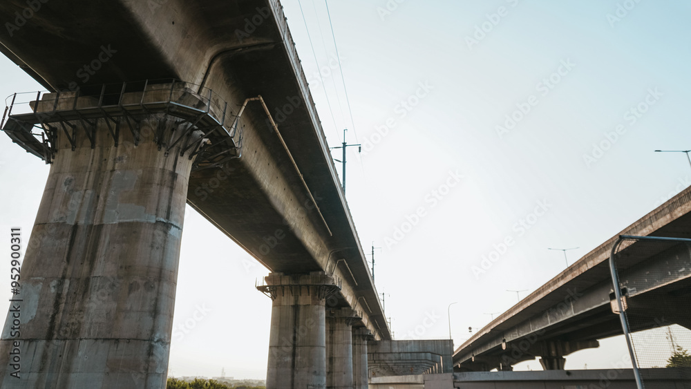 Dramatic underpass view of towering concrete bridges against the sky, capturing modern infrastructure with strong architectural lines and industrial aesthetics Dramatic underpass view of towering concrete bridges against the sky, capturing modern infrastructure with strong architectural lines and industrial aesthetics