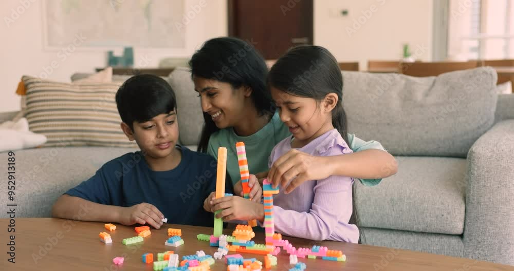 Happy young Indian mom helping cute sibling kids to stack towers from toy colorful bricks, playing learning creative games with son and little daughter in home living room. Nanny watching girl and boy