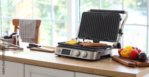 Obraz na plátně Delicious sausages and vegetables in modern electric grill on table at kitchen