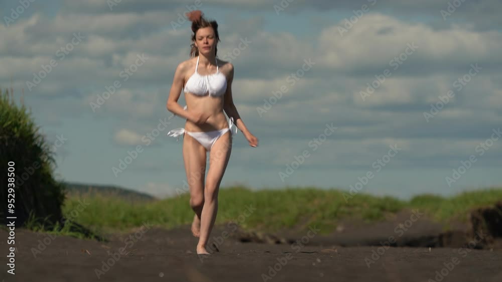 Graceful slim sportive woman dressed in stylish white two piece bikini swimsuit running on sandy beach during summer sports activity in sunny weather. Full length front view, handheld shot, real time Graceful slim sportive woman dressed in stylish white two piece bikini swimsuit running on sandy beach during summer sports activity in sunny weather. Full length front view, handheld shot, real time
