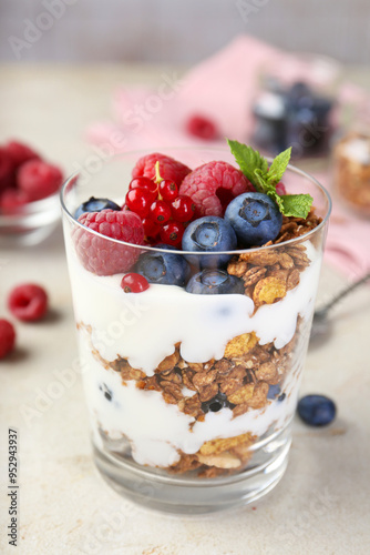 Tasty yogurt with fresh berries, granola and mint in glass on gray textured table, closeup