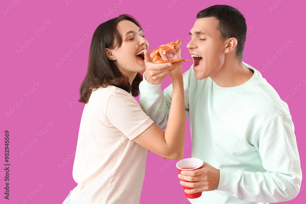 Young couple eating tasty pepperoni pizza on purple background Young couple eating tasty pepperoni pizza on purple background
