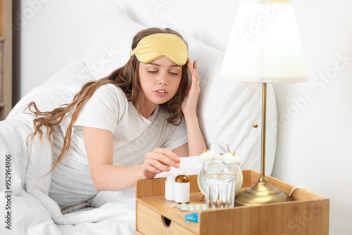 Young woman taking sleeping drops from table in bedroom photo