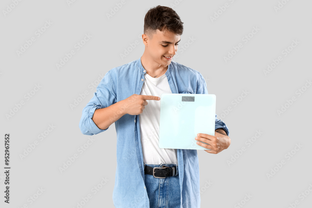 Young man pointing at weight scales on light background Young man pointing at weight scales on light background