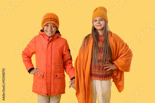 Cute little happy children in winter clothes holding hands on yellow background