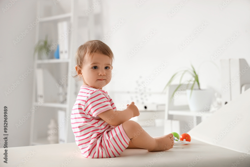 Cute little baby with rattle sitting on couch and visiting pediatrician in clinic Cute little baby with rattle sitting on couch and visiting pediatrician in clinic