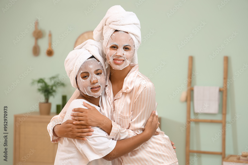 Φωτογραφία Happy young African-American mother and her daughter in pajamas with facial shee