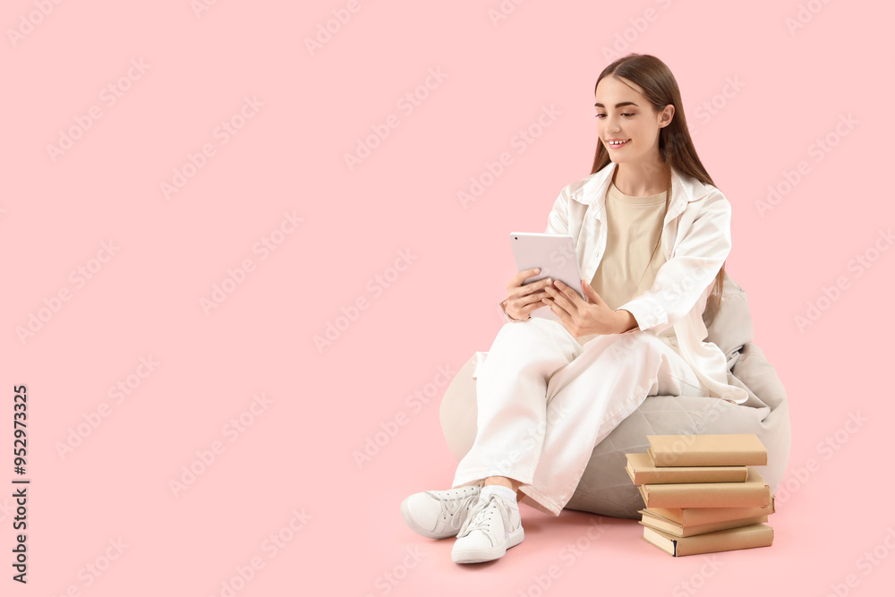 Happy female student with books and tablet sitting on beanbag chair against pink background