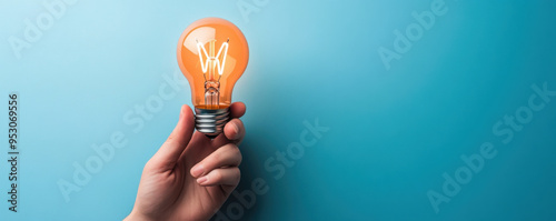 A hand holding a glowing orange light bulb against a blue background, symbolizing creativity, ideas, and innovation.