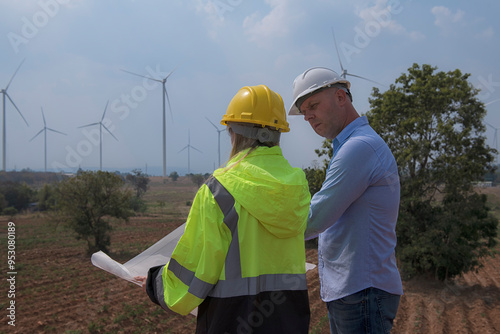 couple worker with helmet discuss job with drawing on wind turbine background.