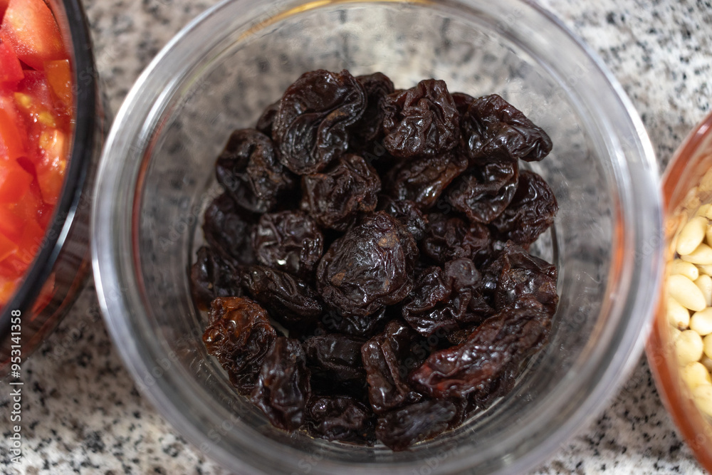 Ingredients to prepare chiles en nogada. Dried prunes in a glass bowl on a marble countertop. Close-up photography of prunes as an ingredient for cooking. Ingredients to prepare chiles en nogada. Dried prunes in a glass bowl on a marble countertop. Close-up photography of prunes as an ingredient for cooking.