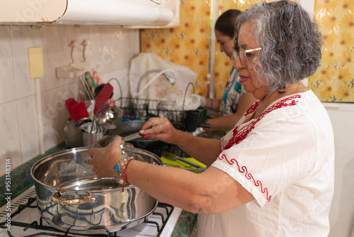 Fotografi Women dressed in traditional Mexican clothing preparing the ground beef filling needed to prepare traditional chiles en nogada in a traditional kitchen