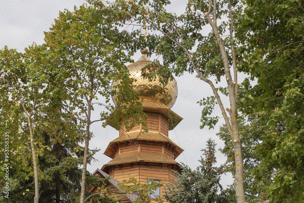 A wooden Russian Orthodox church with golden domes, surrounded by trees and greenery in the city A wooden Russian Orthodox church with golden domes, surrounded by trees and greenery in the city
