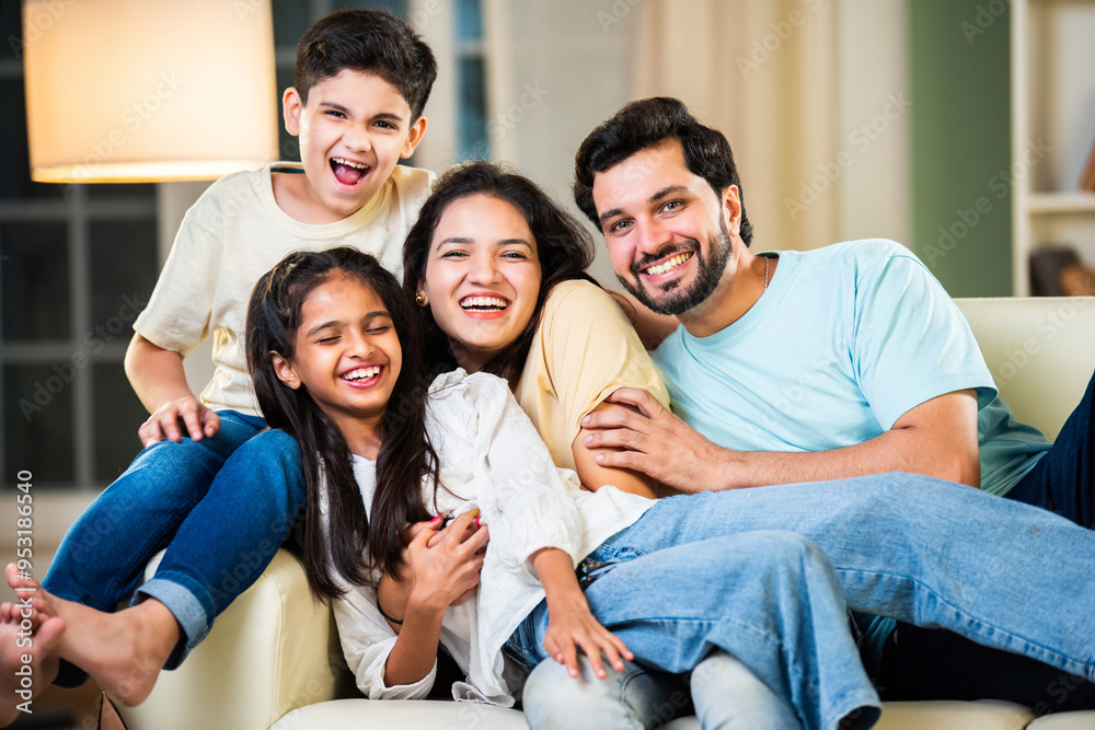 Cheerful Indian parents and kids sitting on the sofa, enjoying playful moments and laughter at home Cheerful Indian parents and kids sitting on the sofa, enjoying playful moments and laughter at home
