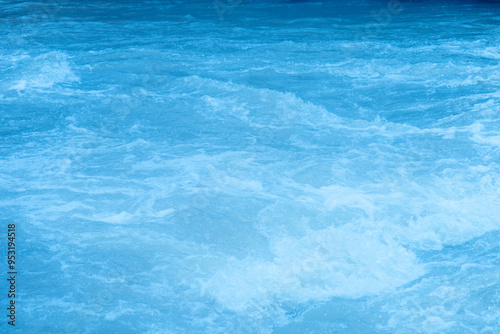 Blue water with ripples on the surface. Defocus blurred transparent blue colored clear calm water surface texture with splashes and bubbles. Water waves with shining pattern texture background.