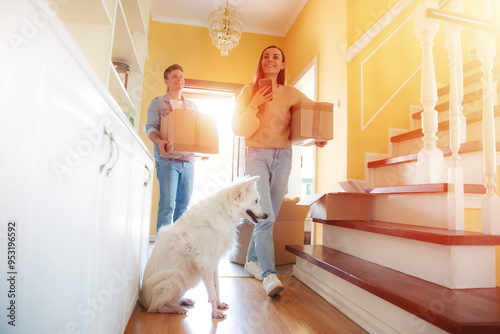 Photography A couple moves into their new home, carrying boxes with smiles as their dog sits attentively by the stairs