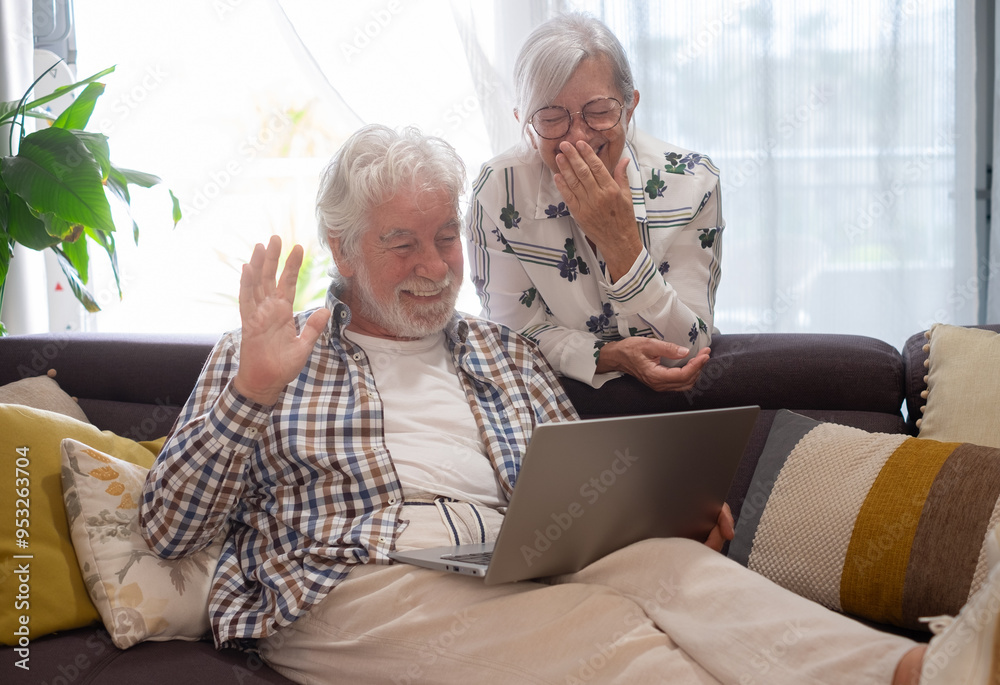 Video call concept. Happy bonding senior retired couple sitting on sofa, using laptop technology for online webcam connection, enjoying carefree moments together with distant family Video call concept. Happy bonding senior retired couple sitting on sofa, using laptop technology for online webcam connection, enjoying carefree moments together with distant family