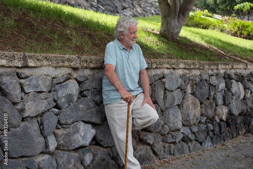 Happy cheerful elder 70s man with walking disability holding knob of cane, leaning on gimp stick walking in the park, suffering from muscles problems, bones disease, recovering after trauma photo