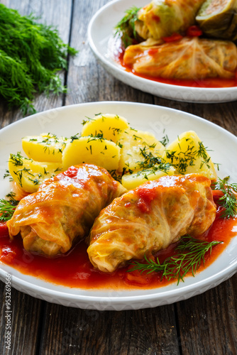 Wrapped minced meat in cabbage leaves served in tomato sauce with boiled potatoes on white plate on wooden table - polish dish golabki photo